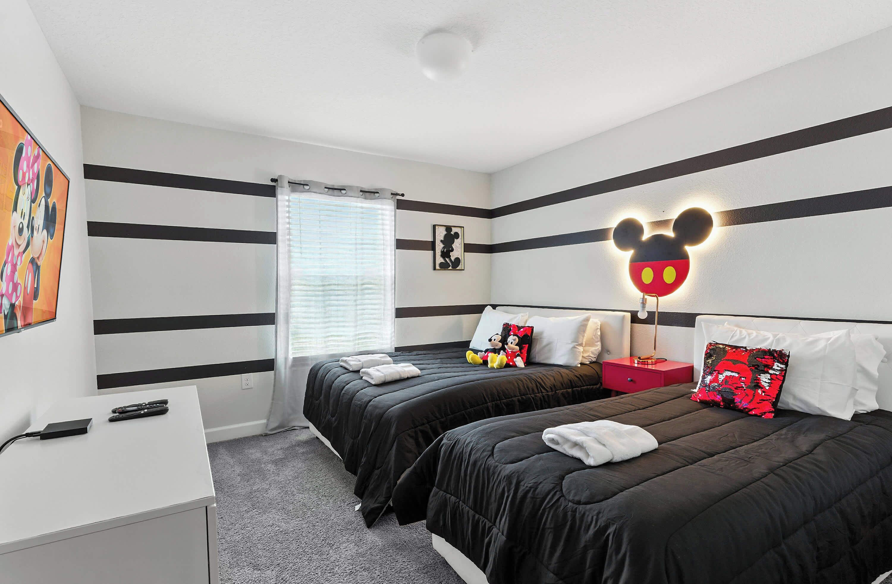 A hotel room with two beds, a desk, and a Mickey Mouse light fixture.