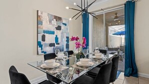 A dining area with a glass table, black chairs, and a modern chandelier. - Champions Gate Oasis, 4BR Vacation Haven (Davenport)