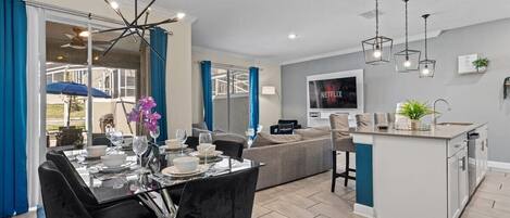 A modern living room with a dining area, a kitchen island, and a TV mounted on the wall.
