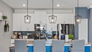 A modern kitchen with white cabinets, a blue island, and three bar stools. - Champions Gate Oasis, 4BR Vacation Haven (Davenport)