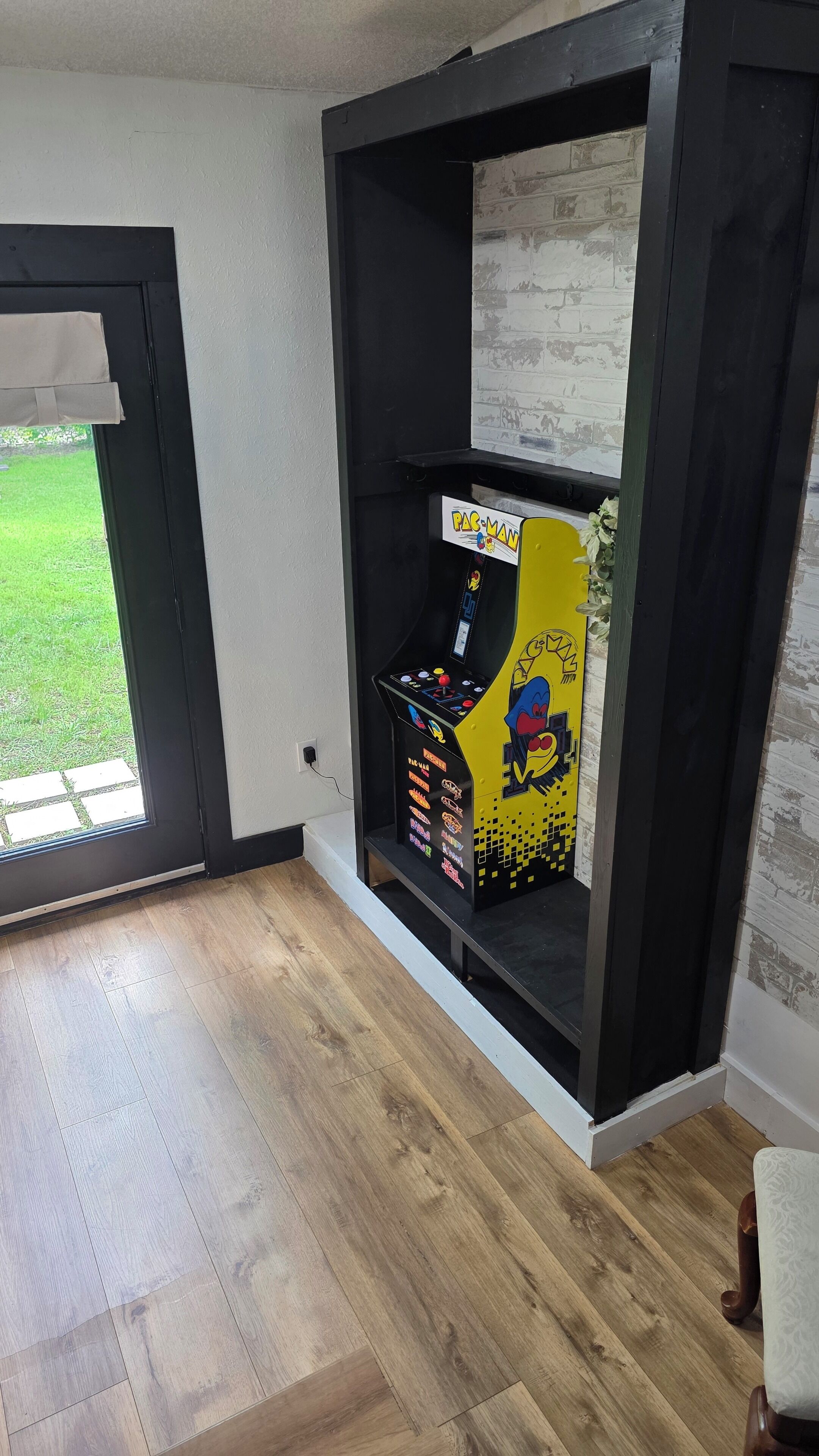 A room with a Pac-Man arcade machine, a door leading outside, and a wooden floor.