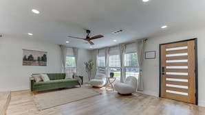 A spacious living room with a green sofa, two white armchairs, a wooden coffee table, and a large window with curtains. - Bright Ivory Studio Getaway- Walk Shops & Dining (Midlothian)