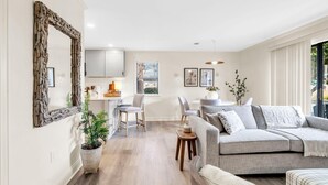 A modern living room with a grey sofa, a dining area with a table and chairs, a kitchen area, and a large mirror on the wall. - Beachwood Villas 1G - The Nest at Seagrove (Santa Rosa Beach)