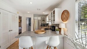 A modern kitchen with white cabinets, a central island with bar stools, a microwave, and a stove. - Beachwood Villas 1G - The Nest at Seagrove (Santa Rosa Beach)