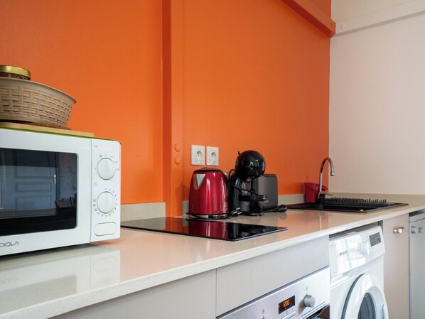 Una cocina con microondas, cafetera y lavadora.