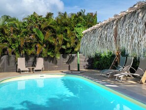 A swimming pool with lounge chairs and a thatched roof structure. - Bungalow Kaz Toumblak in Sainte-Anne (Sante-Anne)