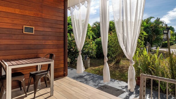 Una terraza de madera con una mesa y sillas, cortinas blancas y un letrero que dice 'Welcome'.