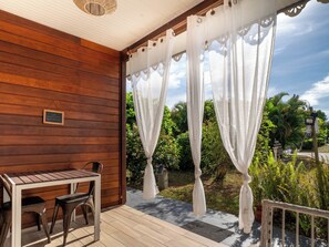 Une terrasse en bois avec une table et des chaises, des rideaux blancs et une pancarte sur laquelle on peut lire « Bienvenue ».