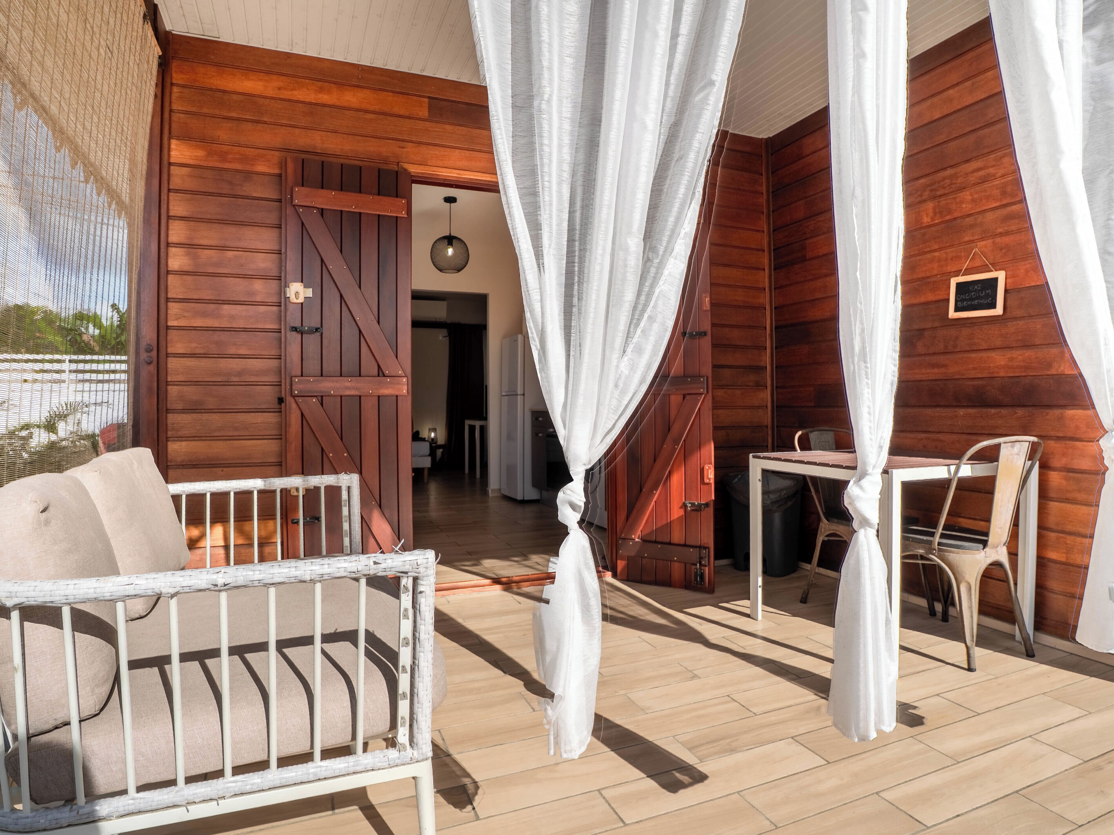 Una baita di legno con un patio arredato con una sedia in vimini bianco, un tavolino e un baldacchino bianco.