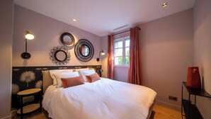 Une chambre à coucher avec un grand lit, un miroir rond, deux appliques murales et une fenêtre avec des rideaux.