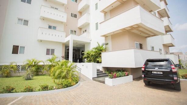 A multi-story residential building with a paved driveway and a parked SUV. - Premium Three Bedroom Apartment at Clifton Place (Accra)