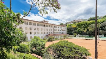 Um edifício com vários andares e telhado plano, com uma quadra de tênis em primeiro plano.