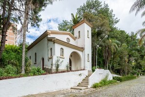 Um edifício branco com um campanário, rodeado por vegetação e um caminho de pedras.