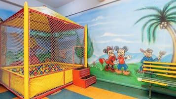 A children's play area with a ball pit, a climbing structure, and a mural with cartoon characters.