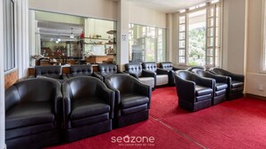 Quarto com poltronas de couro preto dispostas em semicírculo, tapete vermelho e grandes janelas com vista para o verde lá fora.