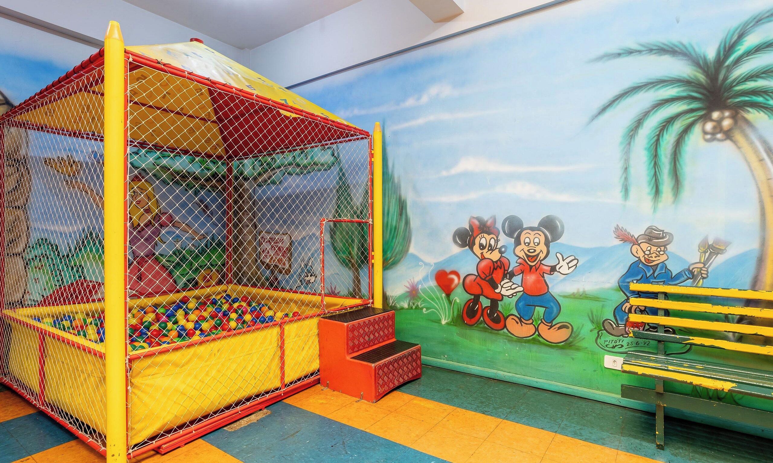 Zona de juegos infantiles con piscina de pelotas y un mural con personajes de caricatura.