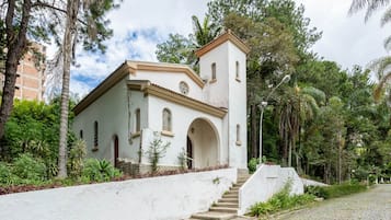 Um edifício branco com um campanário, rodeado por vegetação e um caminho de pedras.