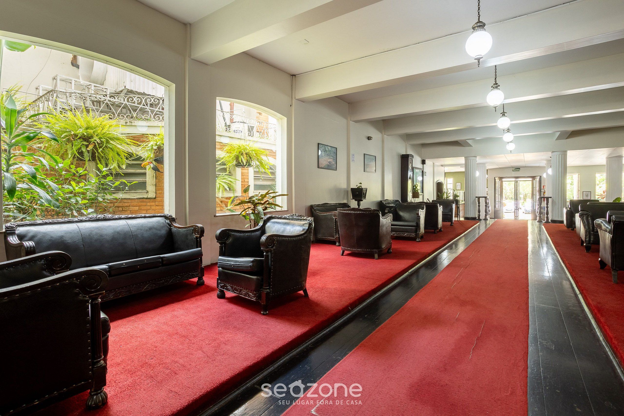A hotel lobby with leather sofas, a red carpet, and a view of the outside.