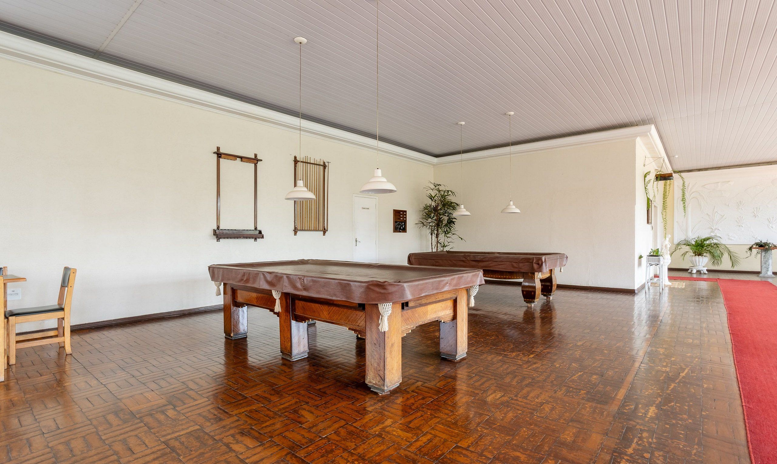 A spacious room with two pool tables, wooden flooring, and a red carpet.