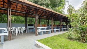 Uma área coberta ao ar livre com mesas e cadeiras, rodeada por vegetação.
