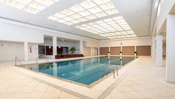 Ein großes Hallenbad mit Dachfenster, gefliestem Boden und einer Holzbank-Bereich.