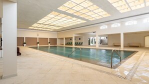Piscina interna com água cristalina, chão em mosaico e teto com claraboias.