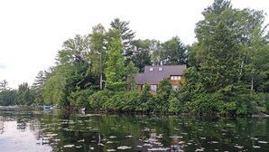 Una casa rodeada de árboles frondosos y un lago con nenúfares.