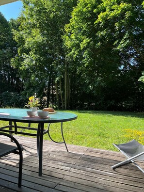 A wooden deck with a round table and chairs, surrounded by lush green trees. - Along the Andlau (Le Hohwald)