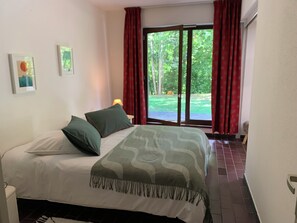 A bedroom with a bed, a nightstand, a lamp, and a view of a garden through a sliding door.