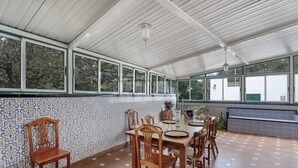 A covered dining area with a tiled floor, wooden chairs, a table, and large windows. - Holiday Home 'Finca Mamposo' – Pets Welcome (Tacoronte)