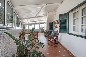 Un portico coperto con pavimento piastrellato, mobili in legno e piante in vaso.