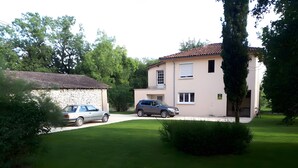 A two-story building with a stone facade and a tiled roof, parked cars, and a well-maintained lawn. - Gîte Chez Jeanne: Shaded Terrace, Private Garden & Wi-Fi in Pern, Quercy Blanc (Pern)