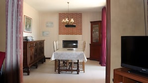 A dining area with a table, chairs, a chandelier, a brick wall, and a television. - Gîte Chez Jeanne: Shaded Terrace, Private Garden & Wi-Fi in Pern, Quercy Blanc (Pern)
