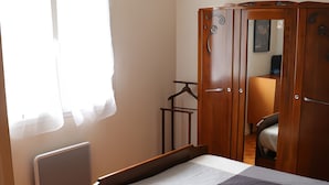 A bedroom with a wooden bed, a wardrobe, a radiator, and a window with curtains. - Gîte Chez Jeanne: Shaded Terrace, Private Garden & Wi-Fi in Pern, Quercy Blanc (Pern)