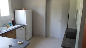 A compact kitchen with a refrigerator, sink, and a small table with a glass and a bottle. - Gîte Chez Jeanne: Shaded Terrace, Private Garden & Wi-Fi in Pern, Quercy Blanc (Pern)