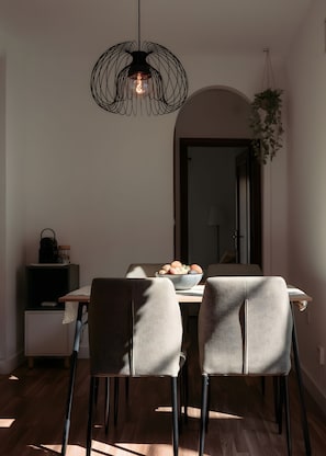 A dining area with a table, chairs, a hanging light fixture, a potted plant, and a doorway.