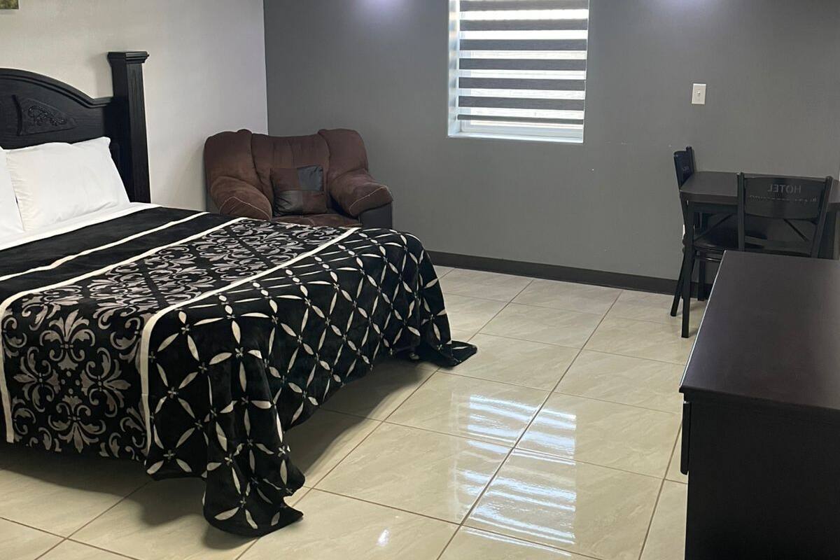 Un dormitorio con una cama, una silla marrón, un escritorio y un cubo de basura.