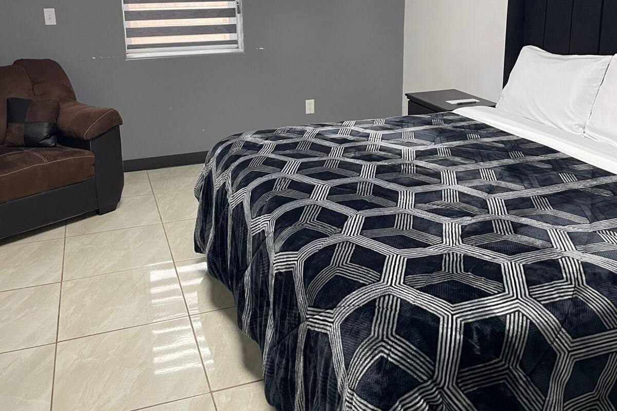 Un dormitorio con cama, un sofá marrón, una ventana con persianas y un equipo de aire acondicionado en la pared.