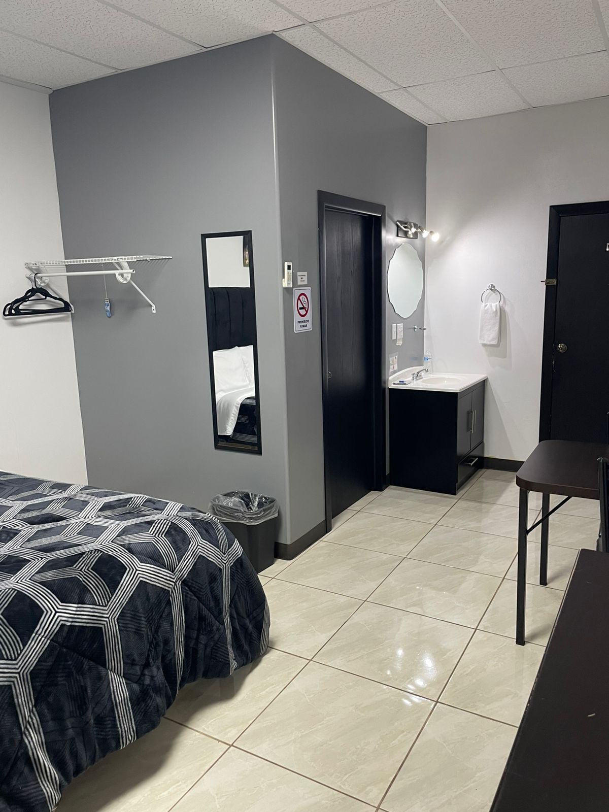 A hotel room with a bed, a bathroom with a sink and mirror, a towel rack, and a trash bin.
