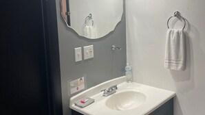 Un baño con lavamanos blanco, muebles oscuros, un espejo grande y una toalla colgada en un perchero.