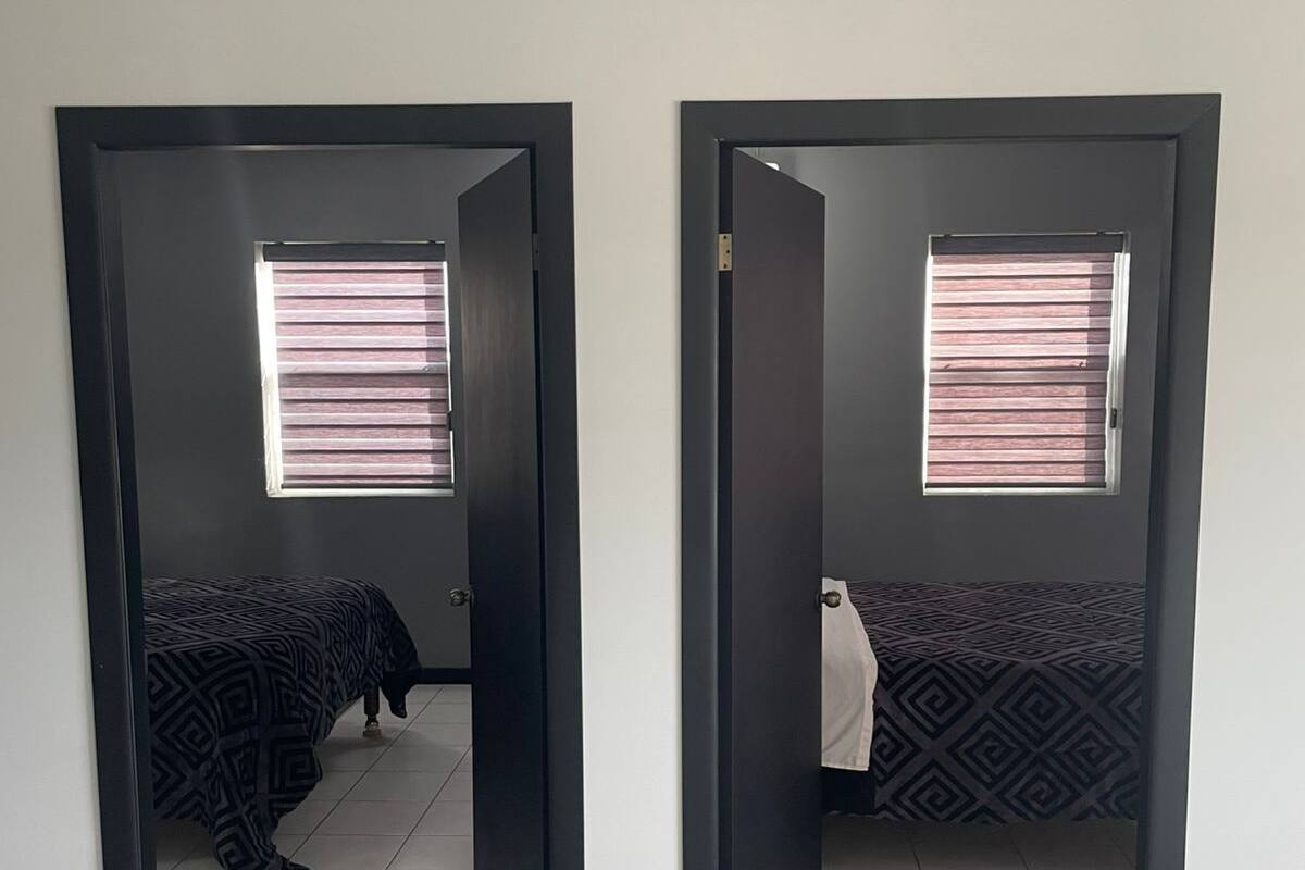 Habitación con dos camas, cada una con ropa de cama estampada, y una ventana con persianas.