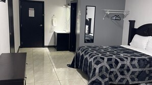 Una habitación de hotel con una cama, un escritorio, un espejo y una puerta.