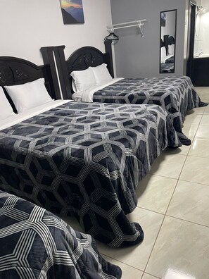Une chambre d’hôtel avec trois lits, chacun recouvert d’une couvre-lit à motifs géométriques.