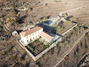 An aerial view of a building with a red-tiled roof, surrounded by a stone wall and palm trees.