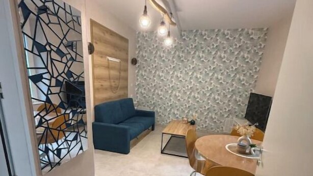 En kompakt opholdsstue med en blå sofa, et spisebord med stole og en væg med et geometrisk mønster.