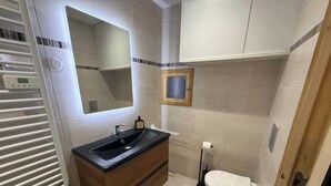 Et lille badeværelse med håndvask, spejl og toilet.