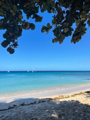 A beach with clear blue water, a sandy shore, and boats in the distance. - Airy 3BR Home with Shared Pool, Close to Beach (Porters, Saint James)