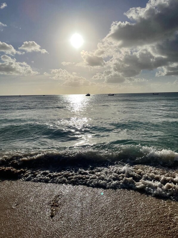A beach with waves, a clear sky, and boats in the distance.