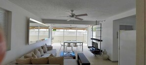 A modern living room with a sofa, a coffee table, a TV, and a dining area with chairs and a table. - Airy 3BR Home with Shared Pool, Close to Beach (Porters, Saint James)