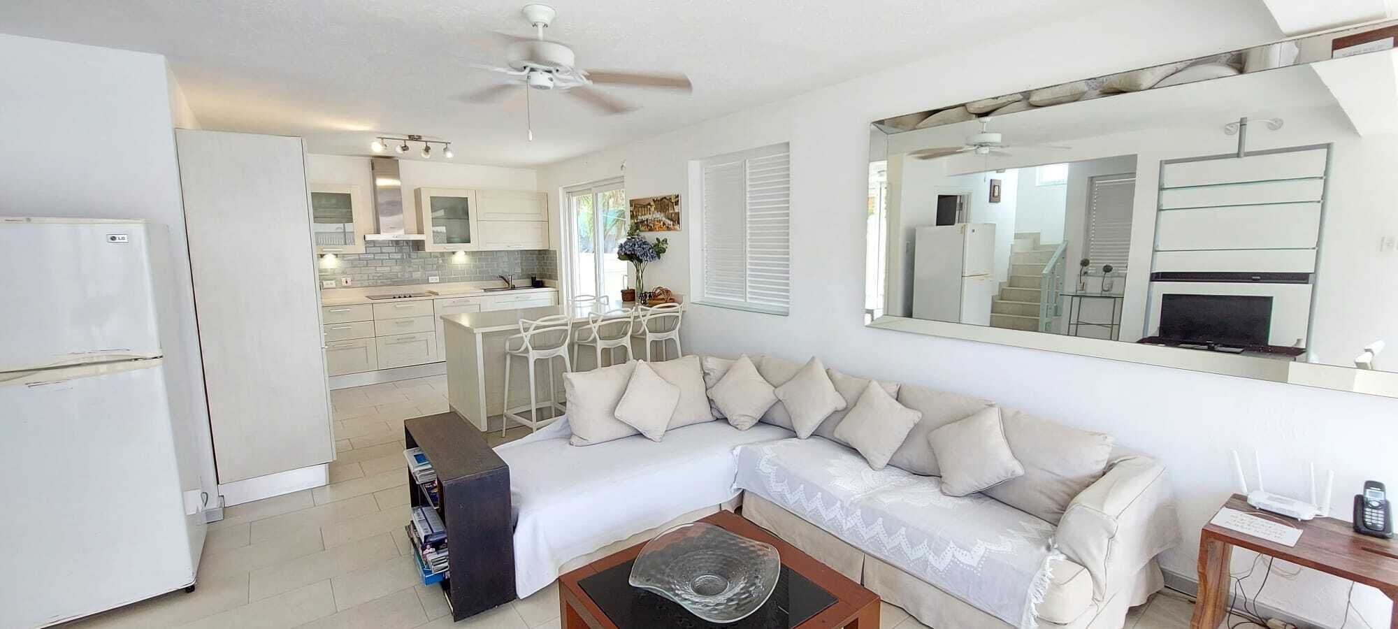 A modern living room with a white sofa, a coffee table, and a dining area with a white table and chairs.